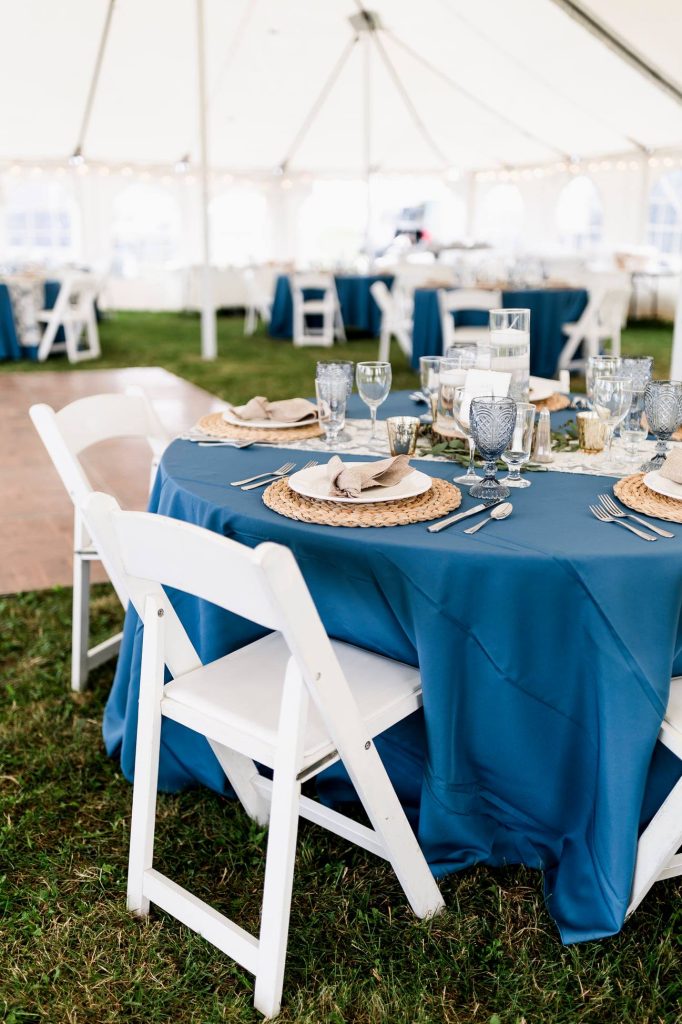 Table setting for outdoor wedding in tent with white folding chairs.
